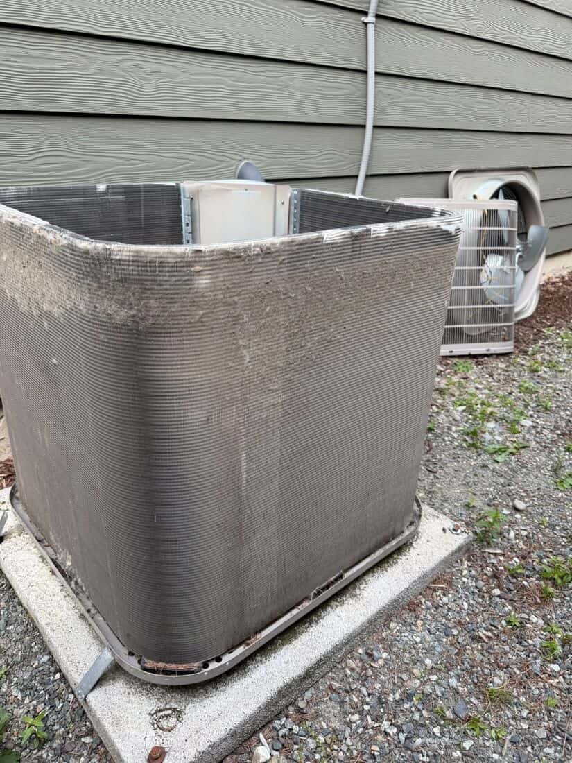 Outdoor condenser cabinet opened up, the coil packed solid with grey yard debris