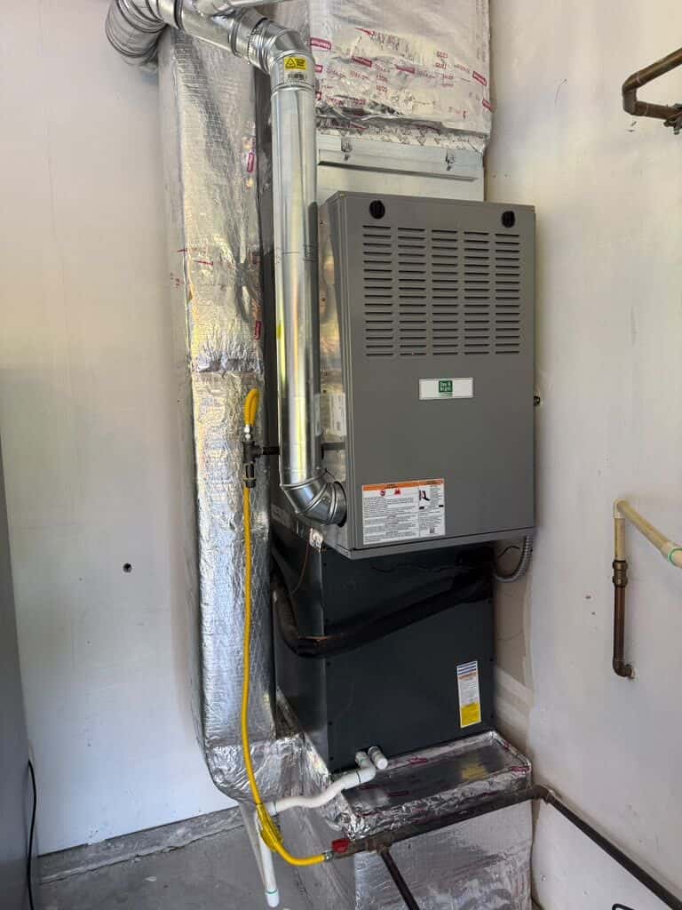Gas furnace mounted on a garage wall with insulated supply plenum and new flue piping
